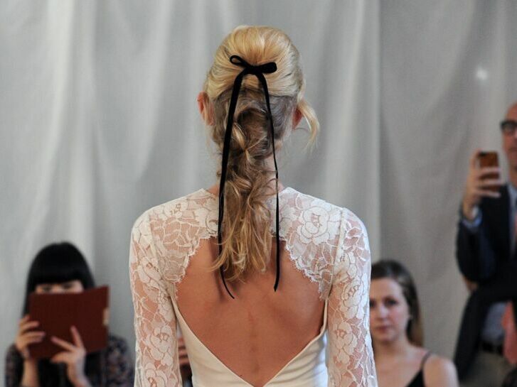 Bride wears her hair in a long braid with a dainty black ribbon. 