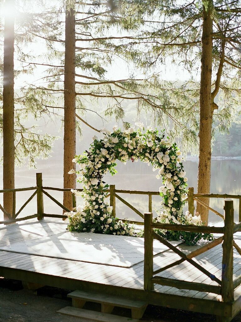 Arch covered in white flowers overlooking woodsy lake