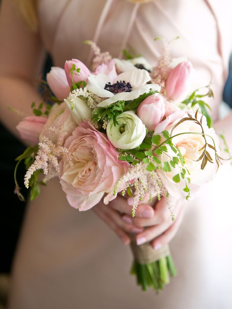A bride holds a bouquet of pale pink roses and white and black panda anemones.