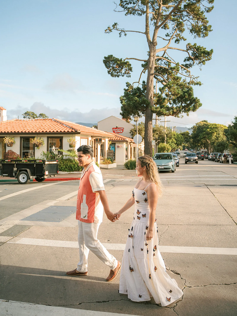 Woman wearing butterfly dress holds hands with fiance in colorful shirt