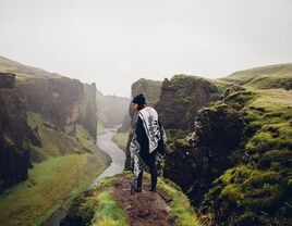 woman standing on green cliff in iceland admiring beautiful mountain scenery