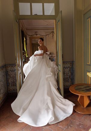 Sposa dress is a voluminous ball gown silhouette, crafted from luxurious mikado fabric that holds its shape beautifully. Available in ivory and light ivory shades, this design is perfect for brides seeking timeless elegance with a touch of grandeur. The dress features a structured yet comfortable lace-up corset that ensures a perfect fit. Hidden pockets add a practical and modern touch to the classic silhouette. The chapel-length train gracefully extends behind, adding a sense of regal sophistication to every step.