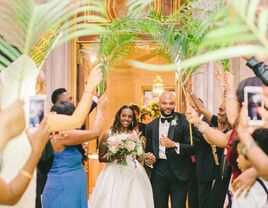 Couple enters their reception while guests wave tropical palm leaf fronds. 