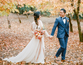 Couple strolling through autumn leaves at their fall wedding
