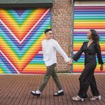 couple holding hands and walking in front of colorful mural for engagement photo shoot 