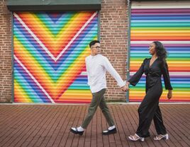 couple holding hands and walking in front of colorful mural for engagement photo shoot 