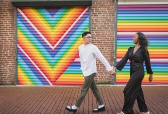 couple holding hands and walking in front of colorful mural for engagement photo shoot 