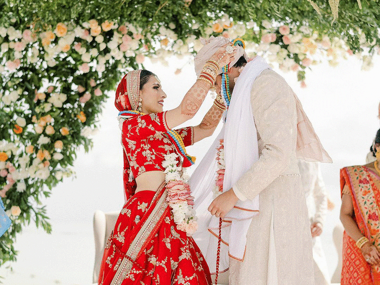 Bride placing mala around groom's neck at Hindu ceremony.