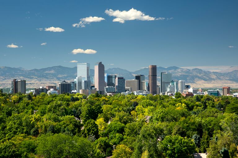 denver city skyline in the summer with the rocky mountains in the backdrop and greenery in the foreground