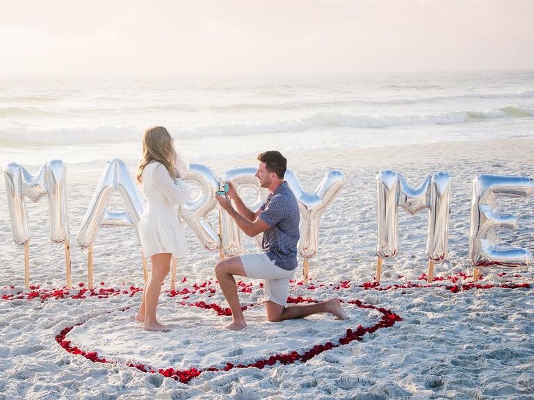 Couple proposal on the beach in front of 'marry me' balloon sign