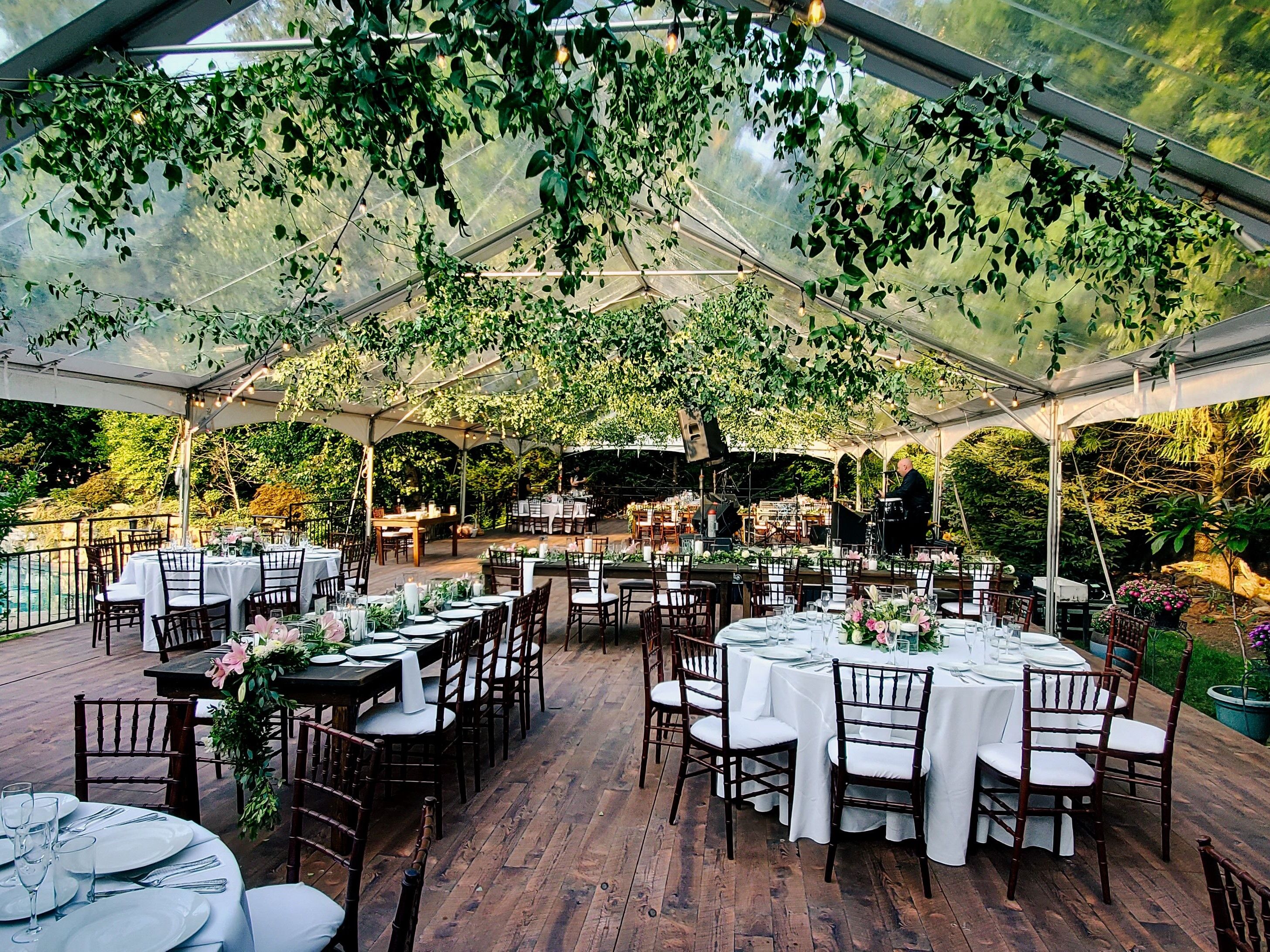 Clear outdoor tent with hanging foliage and brown tables and chairs