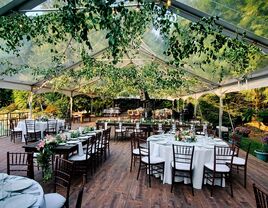 Clear outdoor tent with hanging foliage and brown tables and chairs