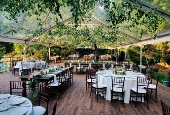 Clear outdoor tent with hanging foliage and brown tables and chairs