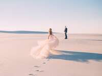 Bride in wedding dress running to husband in sandy desert