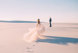 Bride in wedding dress running to husband in sandy desert