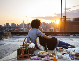 Couple embrace while watching a sunset at a rooftop picnic. 