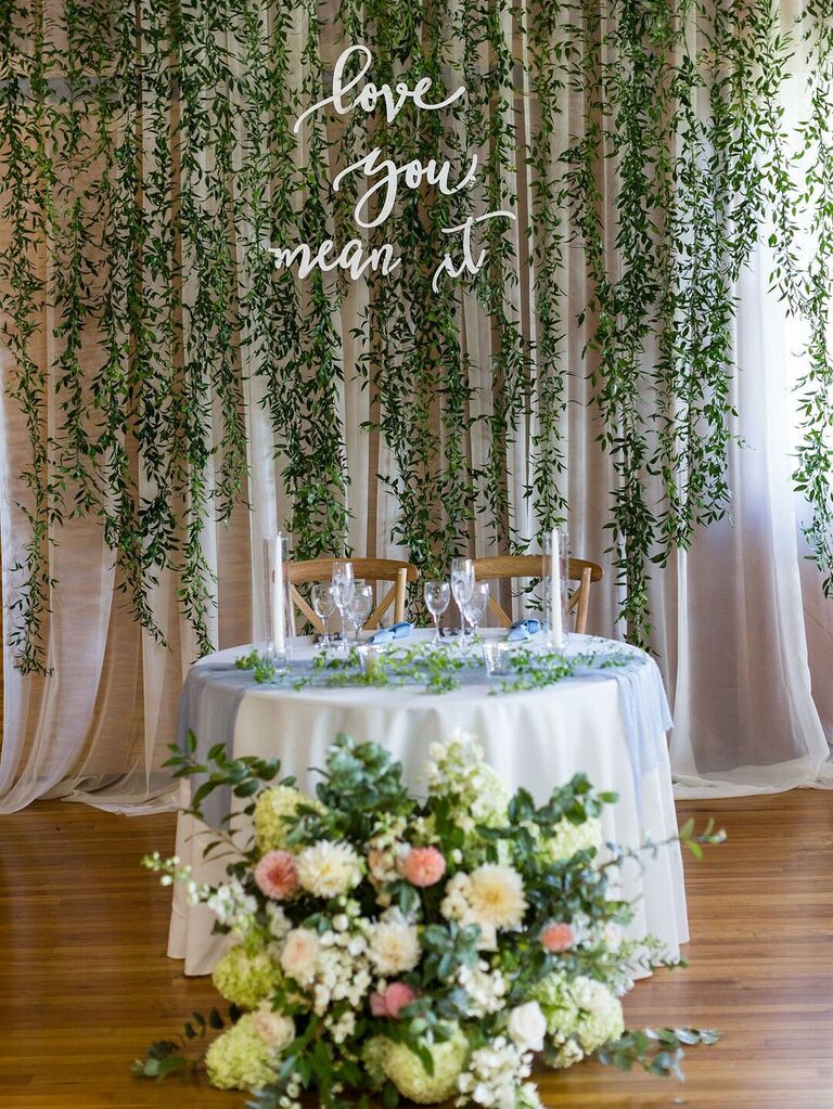 Curtain of hanging vines with neon sign behind sweetheart table at wedding reception