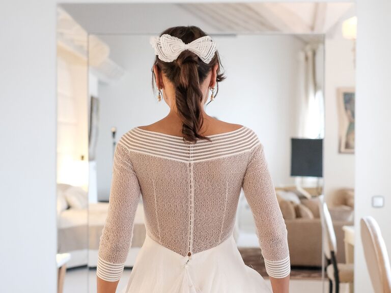 Bride wears her hair in a high ponytail with a white bow. 