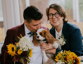 Couple smiling and posing with their Cavalier King Charles Spaniel. 