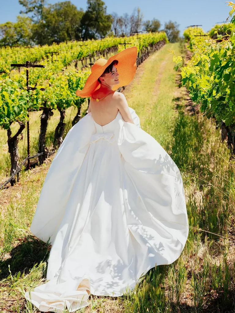 Bride in Strapless Wedding Dress and Oversized Orange Hat in Vineyard