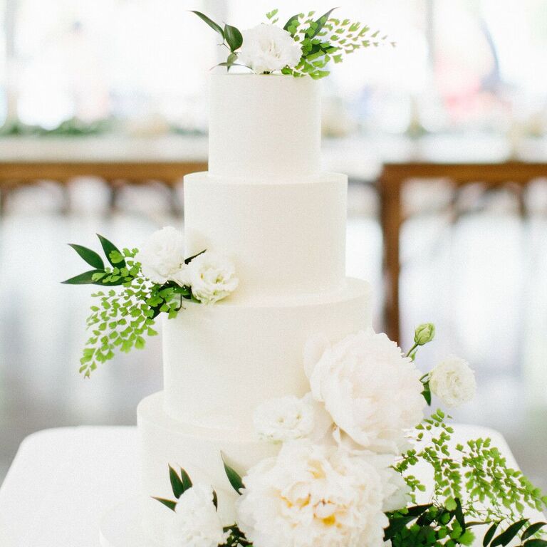 All-white four-tier cake with white flowers and greenery decorations.