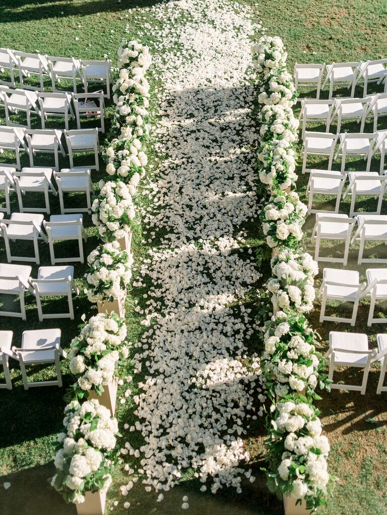 aerial view of outdoor wedding ceremony aisle lined with white flower arrangements along the side and flower petals scattered down the aisle