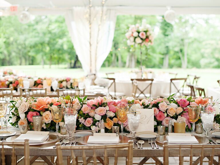 long wooden banquet table decorated with low flower table runner of pink, coral and white roses