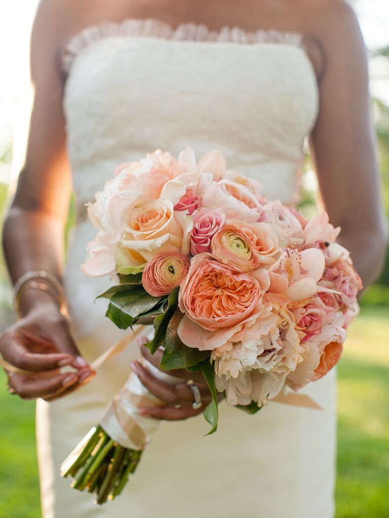 A bride holds a springtime bouquet of peonies in shades of peach and white.