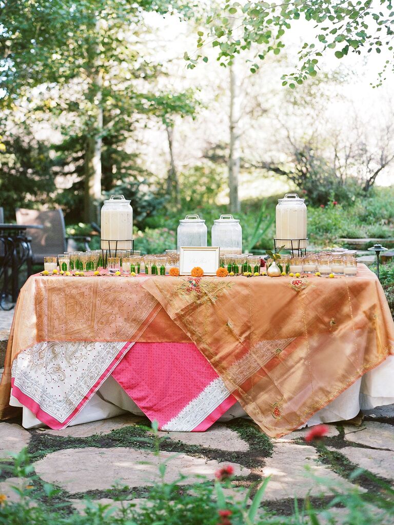 outdoor wedding drink station idea with colorful layered tablecloths and chai tea in dispensers