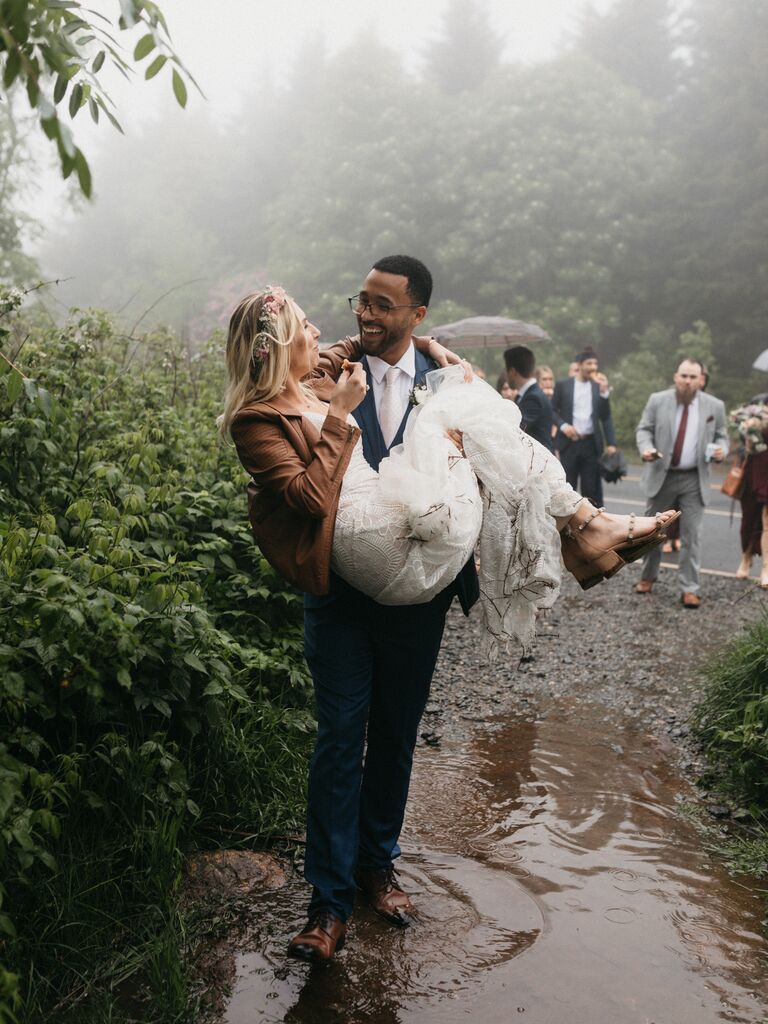 Groom carrying bride through the rain after ceremony