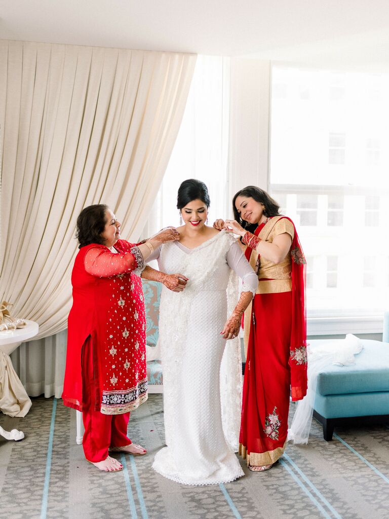 Bride's family helps her put on her wedding outfit. 