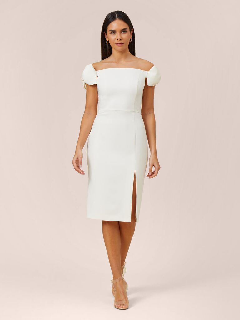 Model wears an elegant mid length white dress with cap sleeves. 