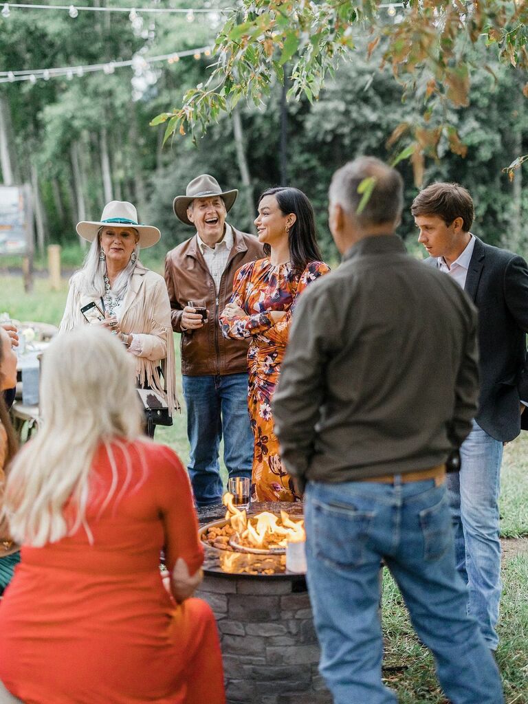 Guests gather around an outdoor fire at a rehearsal dinner. 