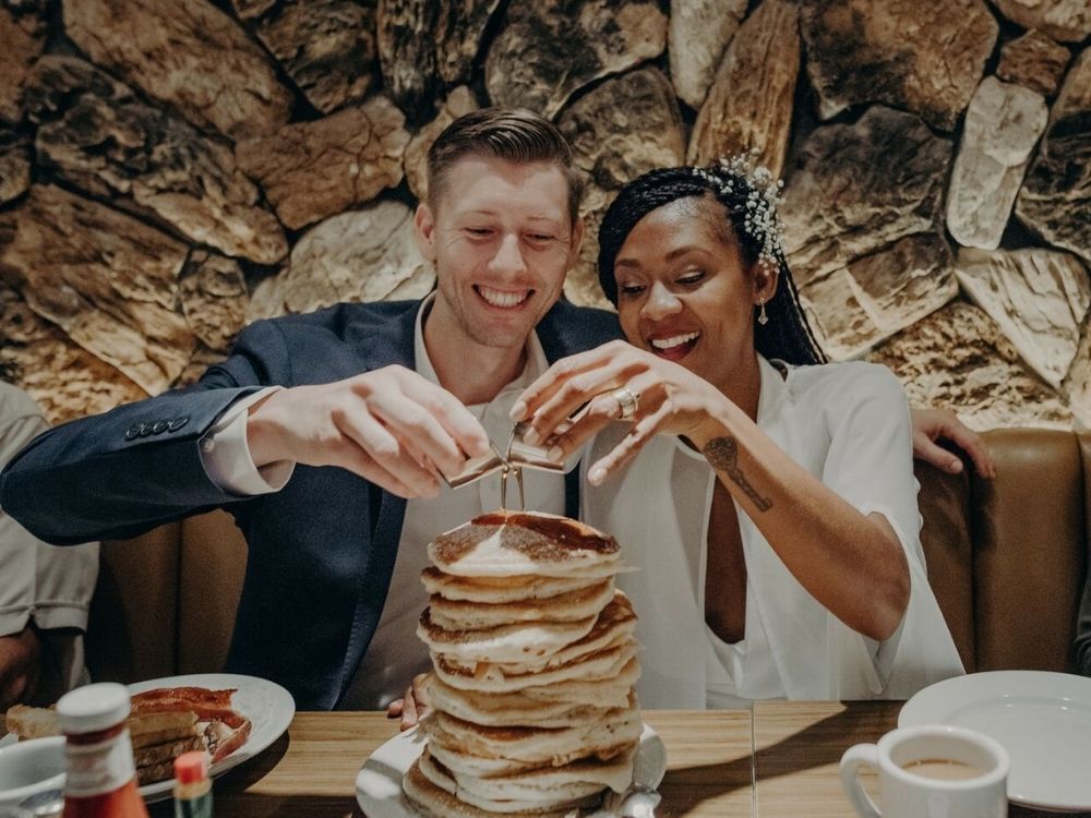 couple pouring syrup on stack of pancakes