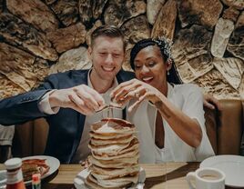 couple pouring syrup on stack of pancakes