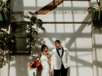 Bride and groom posing in front of white wall surrounded by plants