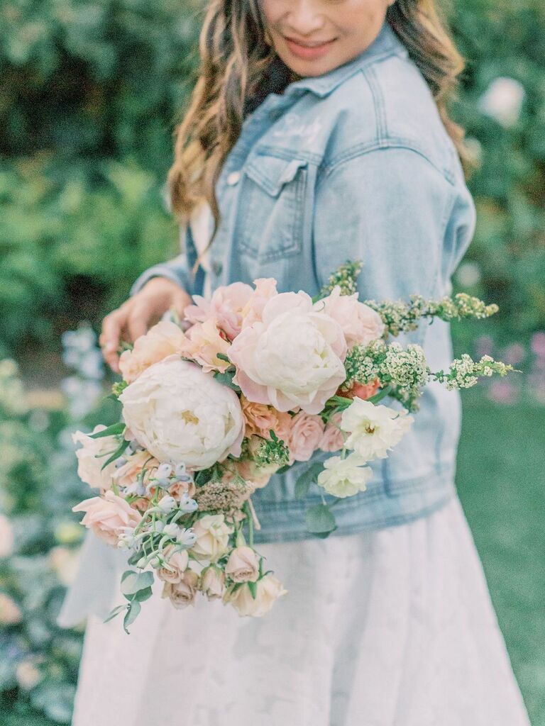 A bride holds a boho-chic bouquet of roses and peonies in pale spring colors.