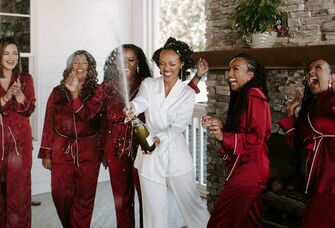 Bride and her bridesmaids pop champagne while wearing matching pajamas. 