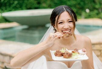 Bride smiles at the camera while eating chicken. 