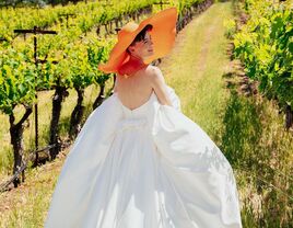 Bride in Strapless Wedding Dress and Oversized Orange Hat in Vineyard