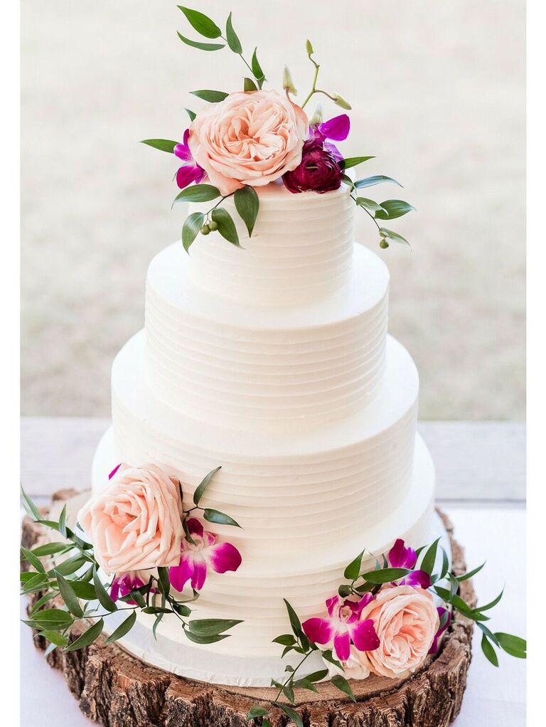 Simple rustic wedding cake with white icing and fresh flowers on tree stump cake stand