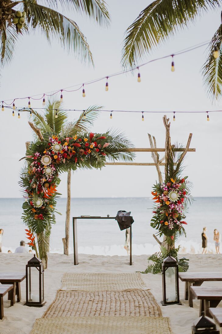Chuppah on the beach covered in protea blooms and tropical leaves. 