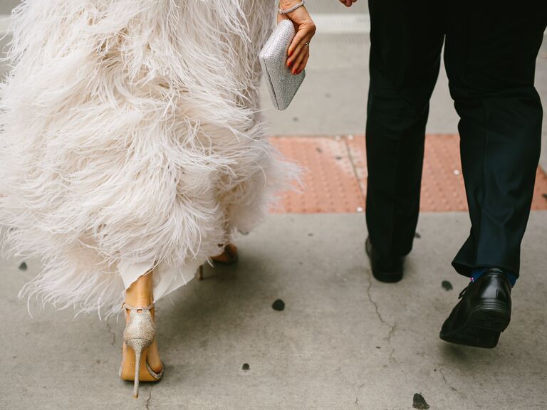 bride wearing feather wedding dress and silver glitter heels walks next to groom down the sidwalk