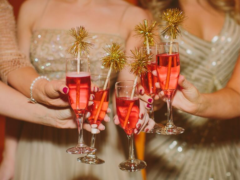 group of bridesmaids holding champagne glasses with gold tinsel pom pom straws