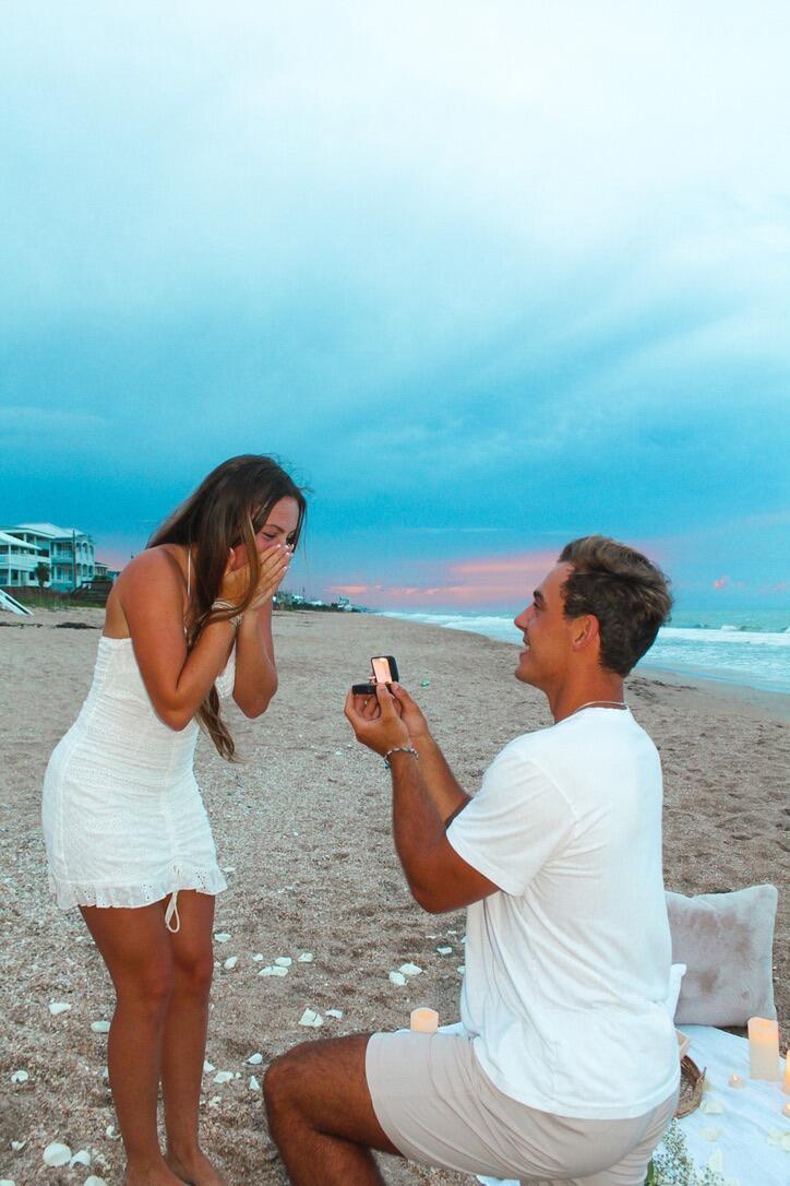 The engagement! Brett proposed to Emma on a beach they visit often near New Smyrna Beach, FL. He laid white rose petals, candles, and all her favorite foods in the sand to make for a beautiful proposal!