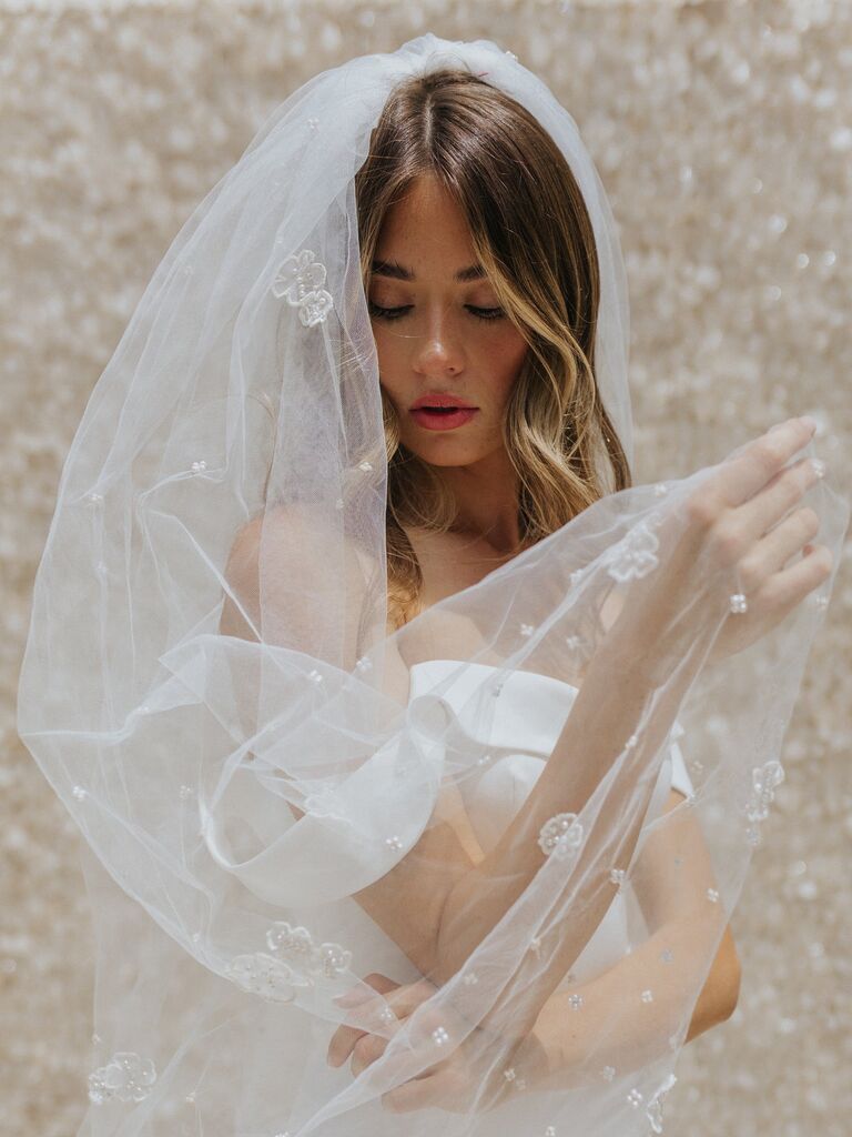 Model wears a flowing sheer veil with pearl accents. 