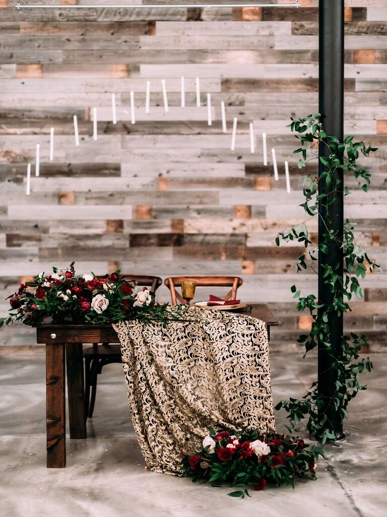 unique sweetheart table idea for harry potter wedding decorated with gold patterned tablecloth, red flowers and floating candles above the table