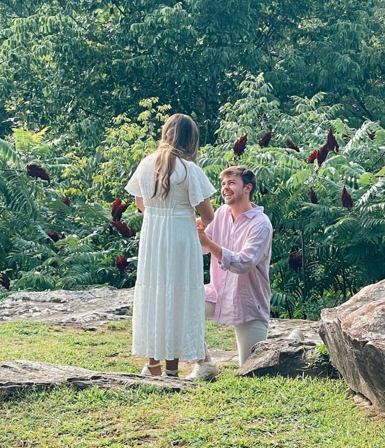 On July 20th, 2024, Wes proposed in a way that reflected their unique love story. Alarie was driven, without knowing what was planned, to the Museum of Fine Arts by her best friend. There, Wes’s sister, Caroline, greeted her with a gift: the program from their first date, a London Lego set, and a heartfelt note from Wes. This was followed by stops at Chick-Fil-A and Target, where more gifts awaited—a meal and The Butt Book. The final destination was Barnes & Noble, where Alarie received the Minecraft Bible and another note. The journey concluded at the overlook on Petit Jean Mountain. As soon as they arrived, Alarie knew what was happening. She saw Wes and their entire family, and he then guided her to the spot where he proposed. They got engaged surrounded by loved ones, in front of God’s beautiful creation.