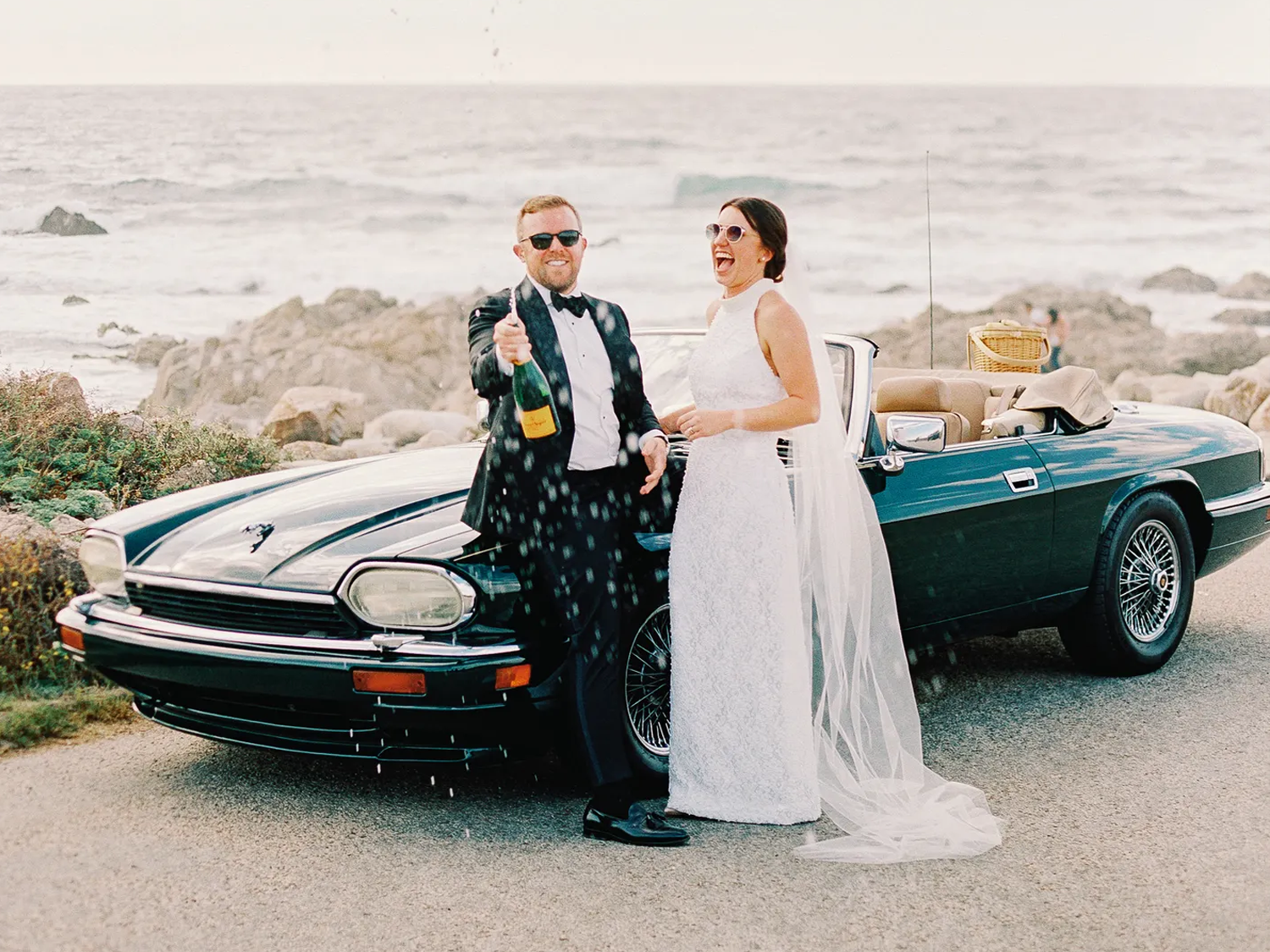 Couple with champagne beside wedding car