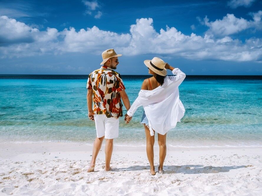Couple holding hand while on a sandy beach looking at the water